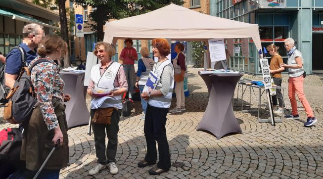Zwei OMAs sprechen vor dem Infostand in der Fußgängerzone mit einem Mann und einer Frau.