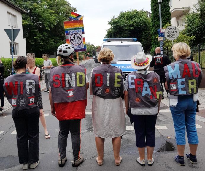 Fünf OMAs nebeneinander von hinten fotografiert: Auf ihren Rücken steht die Botschaft „Wir sind die Brandmauer“