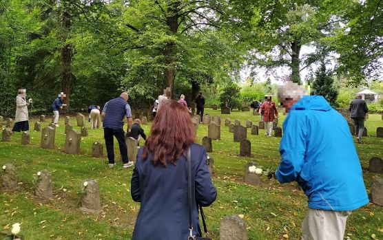 Menschen verteilen weiße Rosen an den Gräbern der Zwangsarbeiter auf dem Nordfriedhof in Hildesheim.