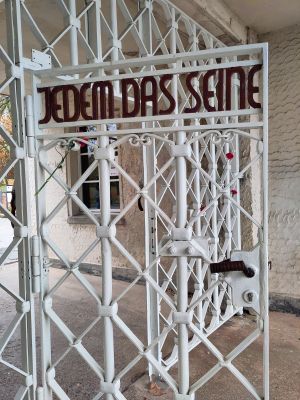 Das Gittertor am Eingang zum Lager. In den weißen Gittern ist in der Tür der Schriftzug „Jedem das Seine“.