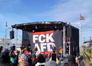 Eine Bühne. Die Band ZSK spielt. Im Hintergrund ist ein riesiges, bühnenfüllendes Banner mit der Aufschrift „FCK AFD“ aufgehängt.