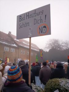 Blick über die Demonstrierenden. Im Hintergrund sieht man einige bunte Fahnen und Plakate aus der Menge ragen. Im Vordergrund ein Plakat mit der Aufschrift: "Bad Harzburg, schäm dich!" Darunter das Wort "No" im Stile eines Verkehrszeichens, das O ist ein stilisierter Hitler-Kopf.