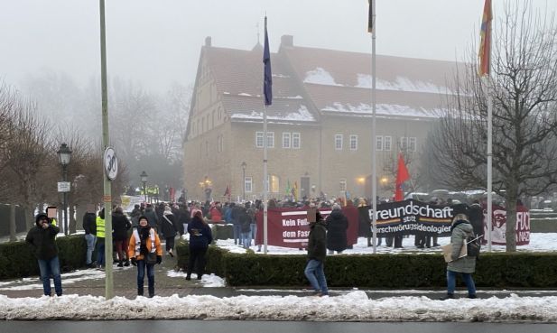 Hinten im Nebel das Bündheimer Schloss, davor die Protestierenden. Man sieht ein großes Banner "Freundschaft statt Verschwörungsideologien". Ein anderes "Kein Fußbreit dem Faschismus".