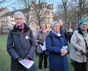 Auf dem Rasen vor der Martin-Luther-Kirche stehen einige OMAS GEGEN RECHTS, die an der Feier zum Holocaust-Gedenktag teilnehmen.