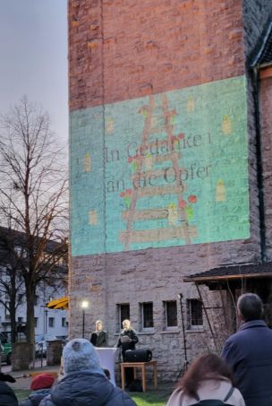 An den Turm der Martin-Luther-Kirche ist ein Bild projiziert: Auf einer grünen Fläche sieht man Bahngleise, die nach hinten führen. Darüber der Text "In Gedanken an die Opfer".