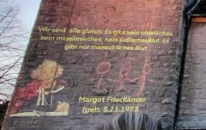 An den Turm der Martin-Luther-Kirche ist ein Zitat von Margot Friedländer, Überlebende des Holocaust, projiziert: "Wir sind alle gleich. Es gibt kein christliches, kein muslimisches, kein jüdisches Blut. Es gibt nur menschliches Blut." Darunter sieht man ein gemaltes Bild von Margot Friedländer, ihr Geburtsdatum (5.11.1921) und drei Strichmännchen.