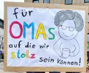 Demoplakat: "für OMAs, auf die wir stolz sein können!" Daneben ist eine ältere Frau mit Kaffeebecher in der Hand gemalt. Die Buchstaben von OMAs und stolz sind bunt.