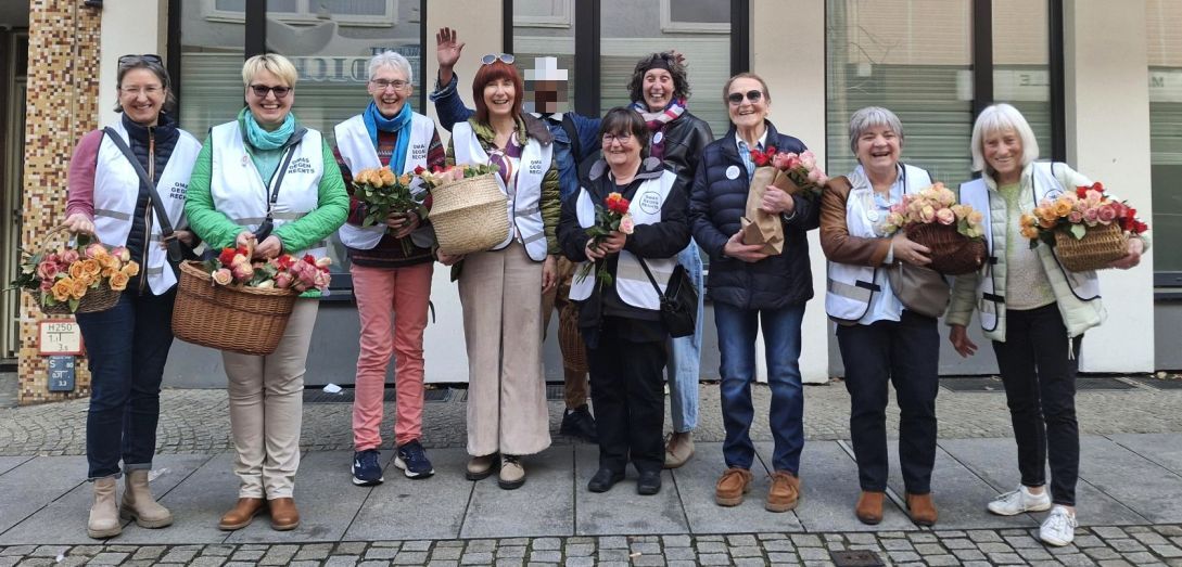 Alles bereit! In einer Reihe stehen die Hildesheimer OMAs gegen Rechts. Sie haben weiße Westen an und Körbe in den Händen, aus denen üppig Rosen in verschiedenen Farben ragen.