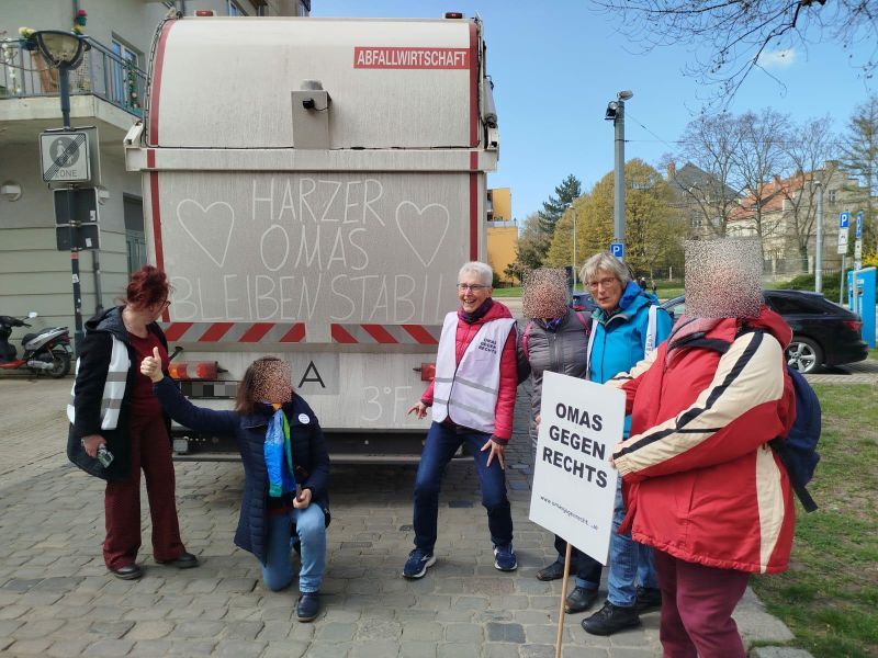 Eine Gruppe von OMAS GEGEN RECHTS hat gute Laune und posiert vor einem Müllwagen, an dessen dreckige Rückseite „Harzer Omas bleiben stabil“ sowie zwei Herzen gemalt sind.