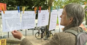 An einer Wäscheleine sind laminierte Texte mit bunten Klammern befestigt. Dazwischen ein Schild mit dem Logo der OMAS GEGEN RECHTS. Auf den Schildern sind Zitate, in denen Menschen beschreiben, wie sie das Kriegsende erlebt haben. Eine Frau liest konzentriert.