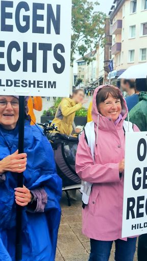Eine OMA im Regen, mit Kapuze auf, aber strahlendem Gesicht.