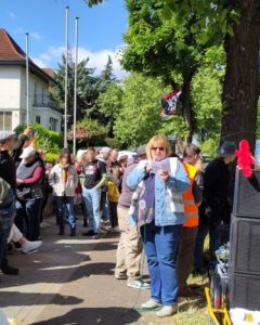 Eine OMA GEGEN RECHTS mit Mikrofon hält eine Rede. Drumherum stehen Demonstranten und hören zu.