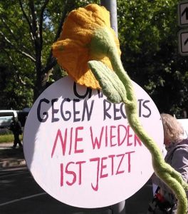 Demoschild, es hängt an einer riesigen gefilzten Blume: "OMAS GEGEN RECHTS. Nie wieder ist jetzt."