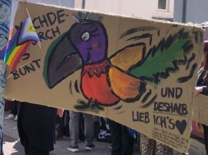 Demoschild: Ein kunterbunter Vogel, daneben steht "Machdeburch is bunt ... und deshalb lieb ich's"