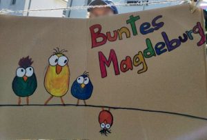 Demoschild: "Buntes Magdeburg", darunter einige bunte Vögel, die auf einer Leine sitzen.
