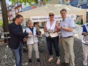Vor dem Stand der OMAS GEGEN RECHTS stehen zwei OMAs sowie Landrat Bernd Lynack und Oberbürgermeister Meyer, die bei den Keksen der OMAS zugreifen.