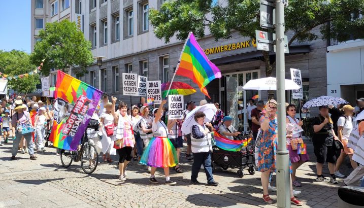 Der CSD-Zug in der Fußgängerzone. Man sieht den Block der OMAS GEGEN RECHTS: Regenbogenfahnen, Regenbogenrock, "Kein Bock auf Nazis", Schilder der OgR.