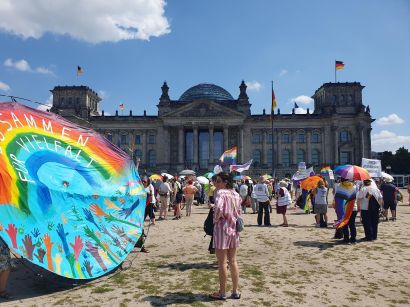 Im Hintergrund der Reichstag, im Vordergrund Teilnehmer:innen der Kundgebung und ein riesiges rundes Stoffbanner mit Regenbogen und der Aufschrift "Zusammen für Vielfalt"