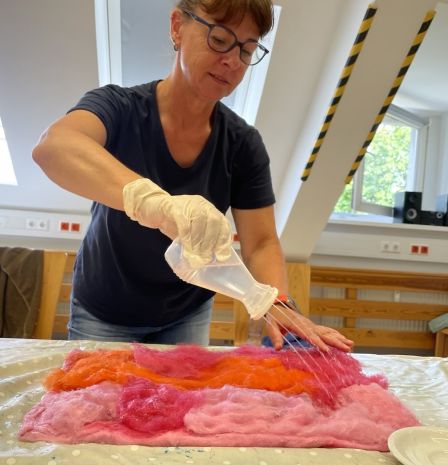 Eine Frau spritzt Wasser auf bunte Wolle, die vor ihr im Rechteck ausgelegt ist.