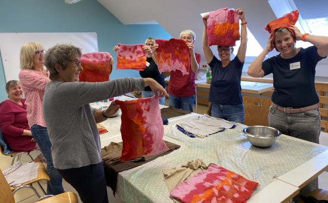 Mehrere Frauen halten ihre Filz-Werkstücke in Rot-Orange-Rosatönen in die Höhe.