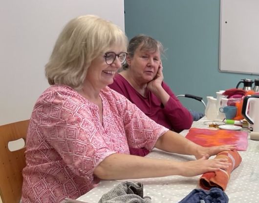 Eine lachende Frau rollt eine Handtuchrolle auf dem Tisch entlang.