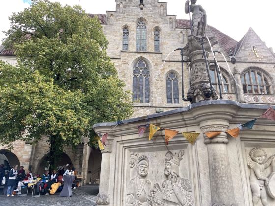 Im Vordergrund der Marktbrunnen, im Hintergrund das Hildesheimer Rathaus. Links davon, unter einer großen Linde, haben sich die OMAs mit ihrem Angebot positioniert.