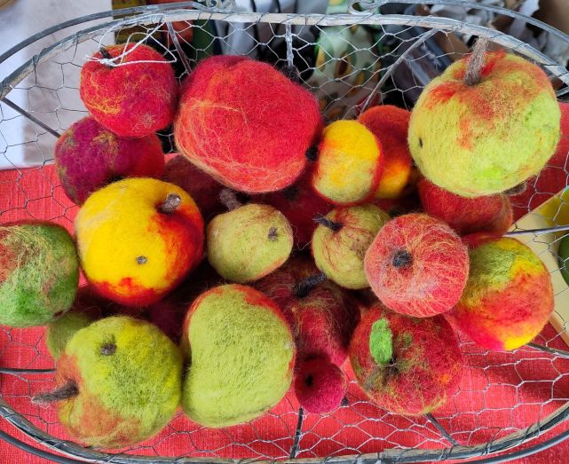 Blick von oben in einen Drahtkorb voll mit gefilzten Äpfeln in vielen Grün-, Rot- und Gelbtönen.