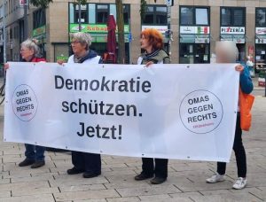 Vier OMAs tragen das Demo-Banner mit der Aufschrift "Demokratie schützen. Jetzt!"
