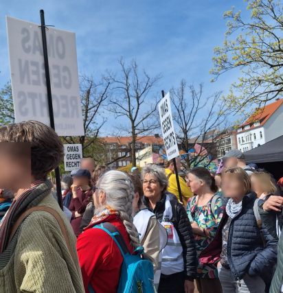 Ausschnitt eines Demonstrationszuges an einem Frühlingstag mit blauem Himme. Einige Teilnehmerinnen tragen Schilder, auf denen OMAS GEGEN RECHTS HILDESHEIM steht.