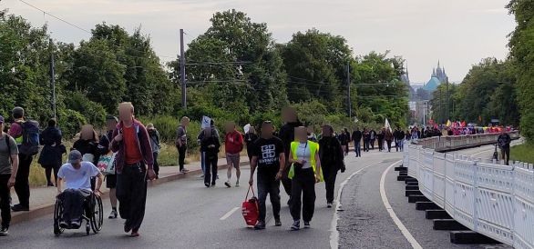 Auf einer großen Straße laufen Menschengrüppchen bergan. Im Hintergrund sieht man zwischen den Bäumen den Erfurter Dom aufragen.