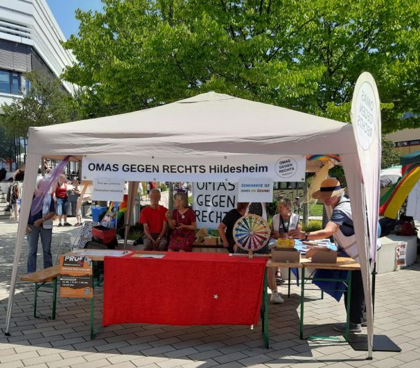 Der Pavillon mit dem Stand der OMAS GEGEN RECHTS Hildesheim. Man erkennt Infomatieral, ein Glücksrad, die Beachflag und mehrere Personen am Stand, teils mit OMA-Westen.