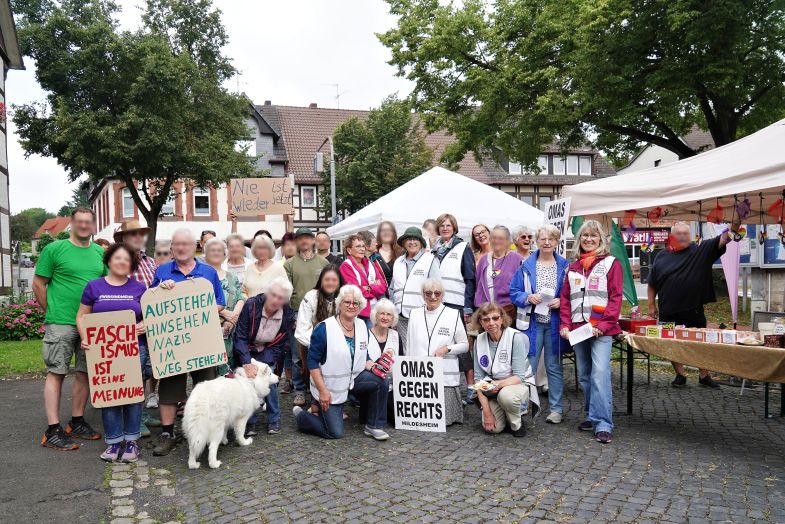 Gruppenfoto mit vielen Menschen, darunter einige OMAS GEGEN RECHTS vor zwei Pavillons. Im Hintergrund Bäume und Fachwerkhäuser.