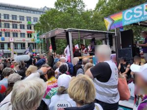 Auf einem Platz hat sich eine Menschenmenge versammelt. Viele Personen tragen die weißen Westen der OMAS GEGEN RECHTS.