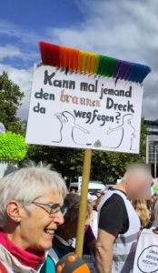 Eine weißhaarige Frau spricht in ein orange-graues ZDF-Mikrofon. Hinter der Frau ragt ein Besen mit regenbogenbunten Borsten in den blauen Himmel, an dem ein Schild hängt: "Kann mal jemand den braunen Dreck da wegfegen?" Unter diesem Text deuten zwei Strichmännchen auf ein braunes Kackhäufchen mit AfD-Logo.