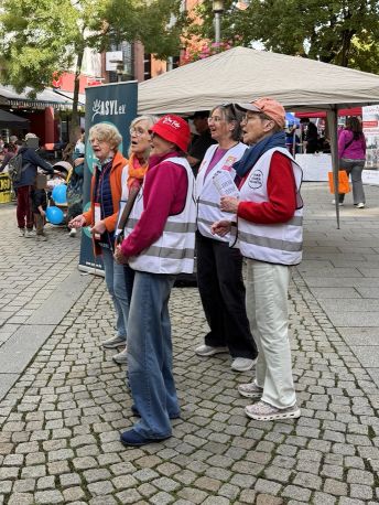Mehreren Frauen mit weißen OMA-Westen stehen in der Fußgängerzone und singen.